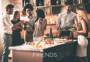 A gathering of friends in the kitchen of a home toasting with wine with the words FRIENDS across the image