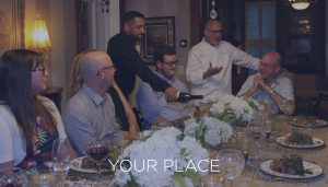 A dining room full of friends served dinner talking with the chef with the words YOUR PLACE across the image